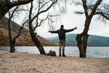 Viajero con los brazos extendidos disfrutando de las vistas junto a un lago en Irlanda