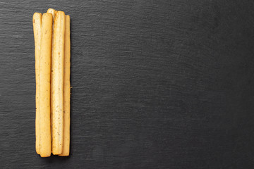 Traditional Italian snack, bread - grissini. On a dark stone table, top view.
