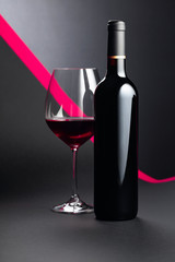Bottle and glass of red wine on a dark background.