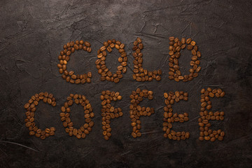 Text cold coffe laid out from coffee beans on a dark concrete background