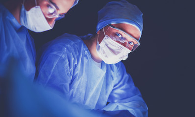 Doctors team in surgery in a dark background.