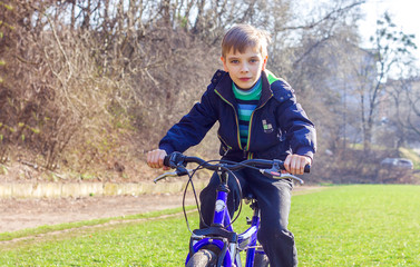 Fototapeta na wymiar A boy sits on a bicycle and looks away, sunny day, outdoor activities happy childhood