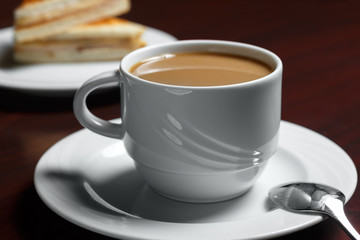A Cup of coffee on the table against the background of a saucer with cakes