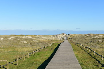 Fototapeta na wymiar Beach with wooden boardwalk and sand dunes with grass and blue sky. Arteixo, Coruña, Galicia, Spain.