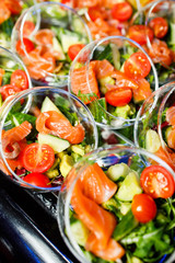 Buffet table with cups with salad of red fish, tomatoes, cucumber