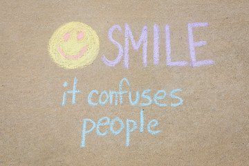 Yellow smiley face made with sidewalk chalk with the words SMILE it confuses people