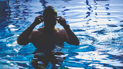 Close-up portrait of a sporty muscular man in swimming goggles and a cap in a swimming pool indoors