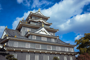 Naklejka premium Okayama, Japan - January 06, 2020: Amazing View to the Japanese Castle via trees under Blue Cloudy Sky