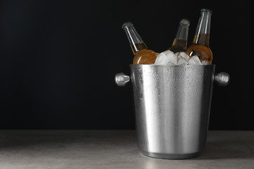 Metal bucket with bottles of beer and ice cubes on grey table. Space for text