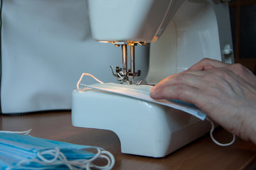 Woman hands using the sewing machine to sew the face medical mask during the coronavirus pandemia. Home made diy protective mask against virus.