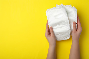 Woman with diapers on yellow background, closeup. Space for text - obrazy, fototapety, plakaty