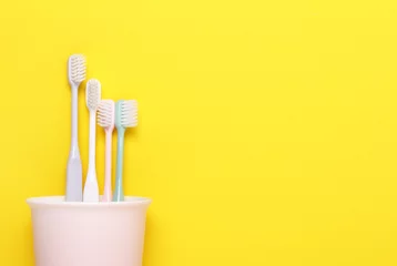 Cup with pink,green,gray and white toothbrushes on yellow background.Taking care of teeth, dental concept. Flat lay photo, copy space, top view.