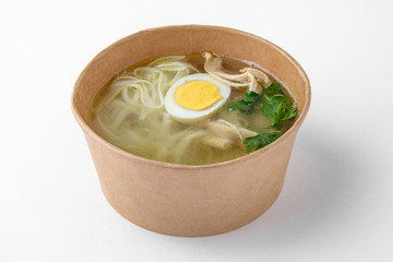 Chicken soup with noodles and egg in a cardboard bowl for take away or food delivery isolated on a white background.