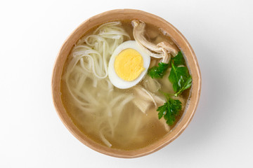 Chicken soup with noodles and egg in a cardboard bowl for take away or food delivery isolated on a white background.