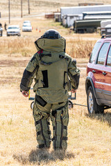 An EOD Bomb Technician with a full bomb suit walks up to a vehicle to search it