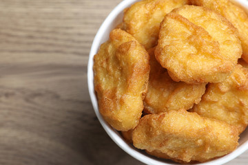 Bucket with tasty chicken nuggets on wooden table, top view