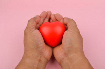 Health concept. Hand holding red heart on pink background. Selective focus.
