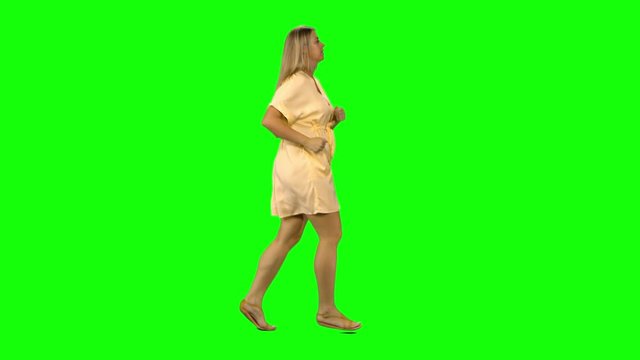Tanned blond woman is running with smile on green screen. Profile view.