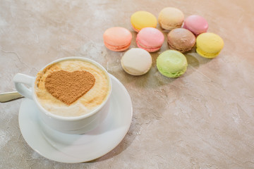 Multi-colored macarons with cappuccino on a table in a coffee shop. Sweet and tasty food