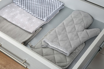 Open drawer with folded towels and oven mittens. Order in kitchen