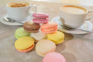 Multi-colored macarons with cappuccino on a table in a coffee shop. Sweet and tasty food
