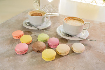 Multi-colored macarons with cappuccino on a table in a coffee shop. Sweet and tasty food