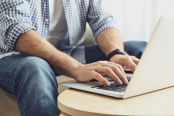 Man working on modern laptop at wooden table indoors, closeup