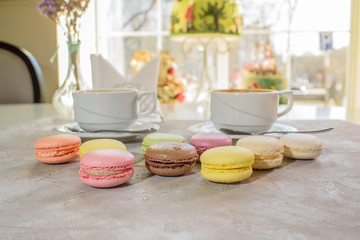 Multi-colored macarons with cappuccino on a table in a coffee shop. Sweet and tasty food