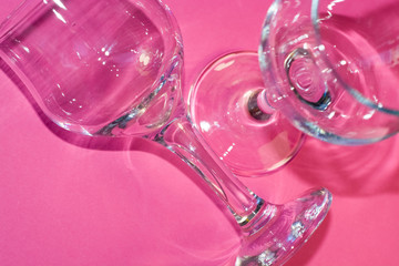 Glass transparent wine glasses on leg on pink background. Highlights and shadows on the dishes.