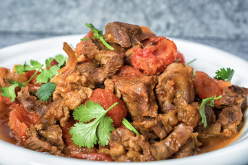 Veal stewed with vegetables in tomato sauce on a black concrete or stone background.