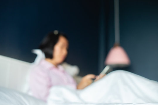 blurred image of asian woman in pajamas is using the internet from a smartphone on a hotel bed.