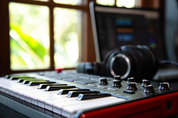 Midi keybard in a music producer home studio, desk with headphones and a notebook. Window with...