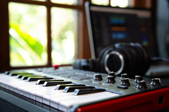 Midi keybard in a music producer home studio, desk with headphones and a notebook. Window with nature in the background.