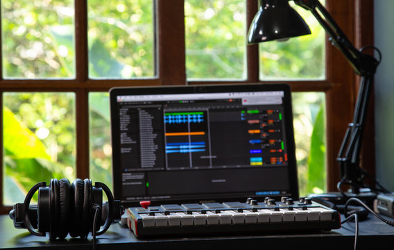 Music producer home studio, desk with headphones, notebook and Midi. Window with nature in the background.
