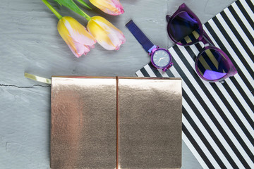 A gold notebook with women's shoes, tulips, glasses and a watch on a concrete background. Flet lay © Вася Фаевич