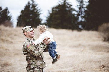 Shallow focus shot of a smiling American soldier carrying his baby