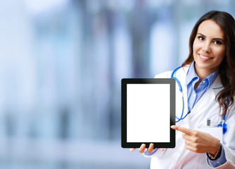Portrait of happy smiling young female doctor showing no-name tablet pc with blank copy space area for some slogan or text, over blurred office background. Medical call center concept picture.