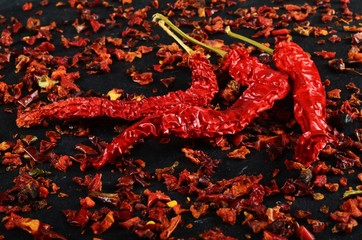chili flakes and dried chili peppers on a black stone background
