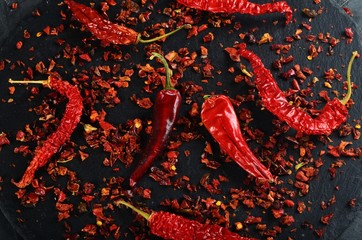 chili flakes and dried chili peppers on a black stone background