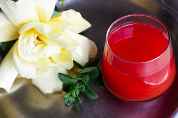 Red orange juice o grapefruit juice in a glass on steel plate with mint leaf and yellow rose. Top view. Vitamin drink for immune defenses.