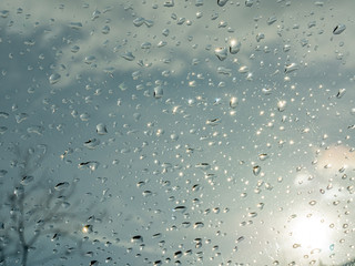 Wet window with rain drops and a cloudy sky outside.