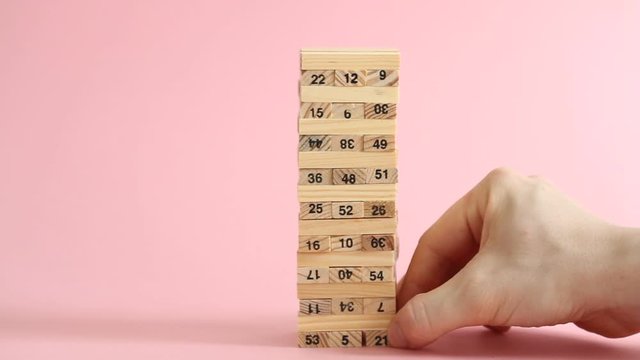 Woman and man plays jenga on pink background. Family recreation and holidays concept.