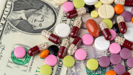 The concept of making money on medicines. Multicolored drugs on a background of dollars. Different remedy, pills, capsule, antibiotic and vitamin.