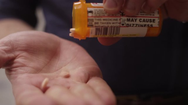 Close-up of a pills getting poured in a man's hand, he takes them