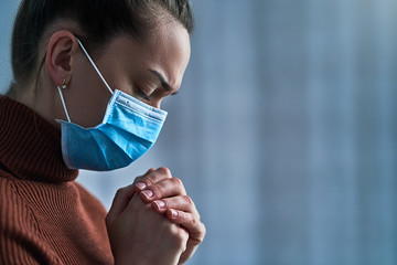 Woman in protective mask with closed eyes and praying hands, asks god for healing and recovery...
