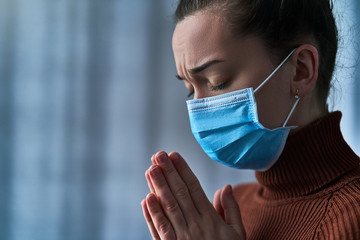Woman in protective mask with closed eyes and praying hands, asks god for healing and recovery during disease, health problems, coronavirus outbreak and flu covid-19 epidemic. Faith and hope