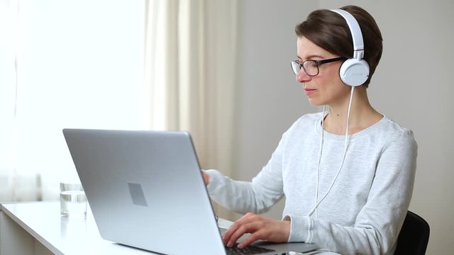 A woman in headphones is studying at home online through video chat on a laptop. The girl friendly advises on a wireless video call. 