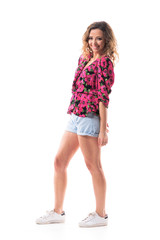 Relaxed happy young curly hair woman in summer wear smiling and looking at camera with arms down. Side view. Full body isolated on white background. 