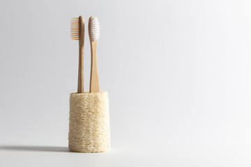 Two toothbrushes made of natural wood are turned away from each other inserted into a natural ecological loofah. on white background. - obrazy, fototapety, plakaty