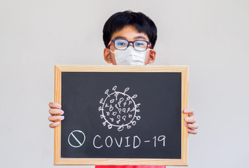 Little boy wearing mask for protect Covid-19, dirty air pollution and PM2.5 and show stop hand gesture for Covid-19 virus outbreak. And holding a blackboard with the words Covid-19. 